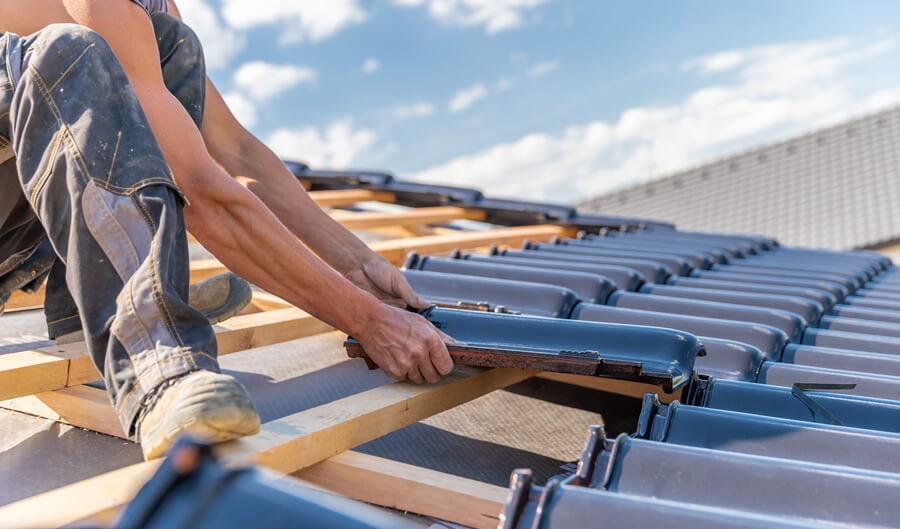 A worker from Titan Exteriors is applying blue roofing tiles on a roof, showcasing skilled roofing installation.