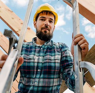 A man in a hard hat and plaid shirt stands on a ladder, representing Titan Exteriors.