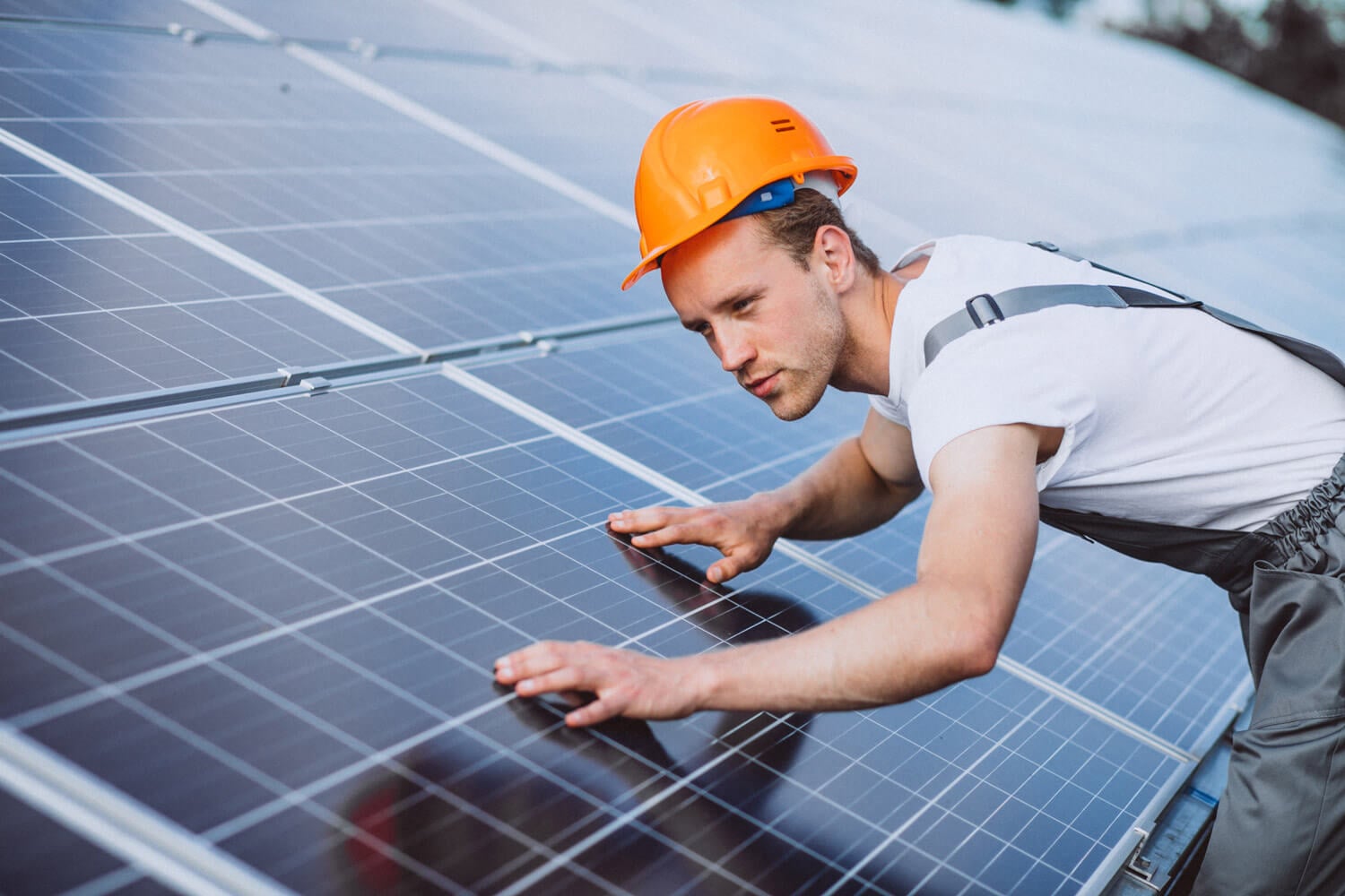 A worker in overalls and a hard hat is installing solar panels for Titan Exteriors on a sunny day.