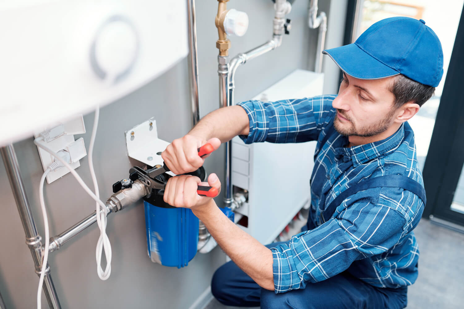 A man in blue overalls repairs a water heater, representing Titan Exteriors' plumbing services.